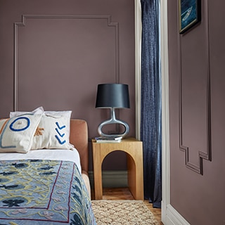 A paneled bedroom with a wooden side table with a fun circular lamp, bed with colorful linens, and a woven accent rug.
